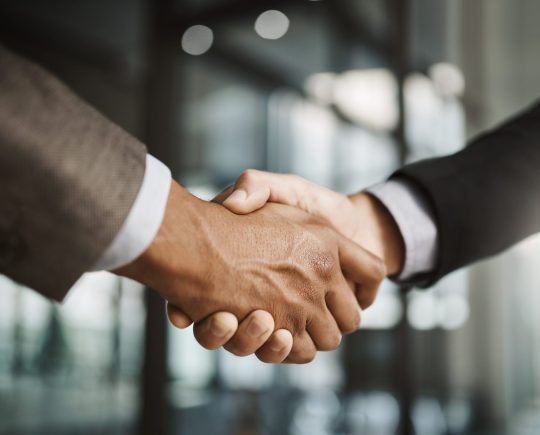 Closeup of business men giving handshake, hiring an employee and welcoming to a company in a meeting in a modern office together. Corporate professionals making deals, agreements and showing teamwork